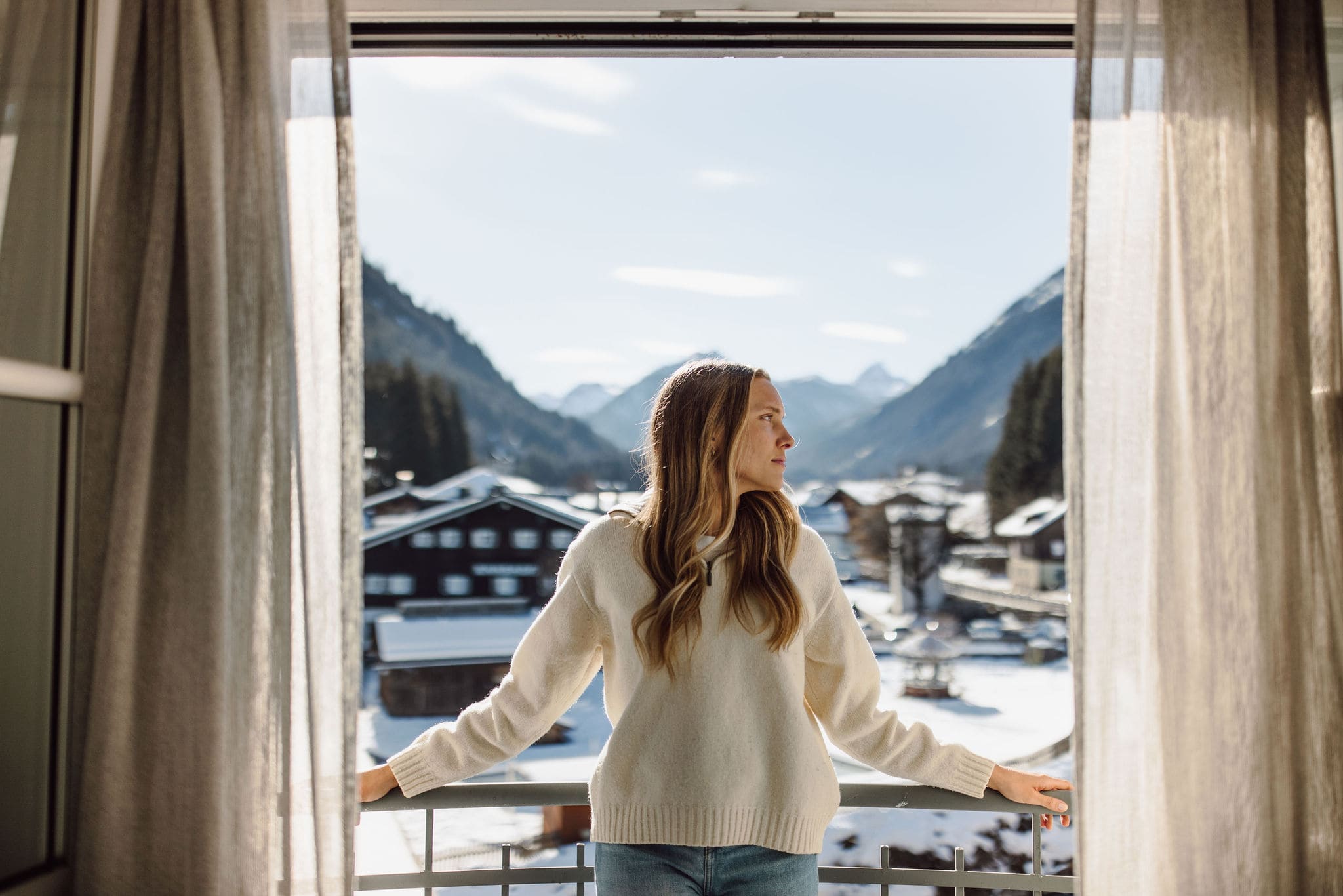 Frau steht auf Balkon und blickt auf verschneite Berglandschaft