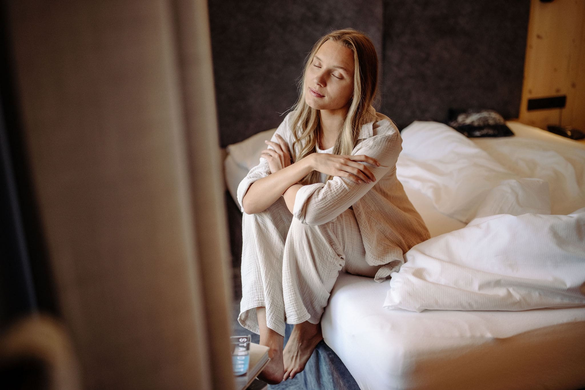 Frau sitzt verträumt auf einem Hotelbett
