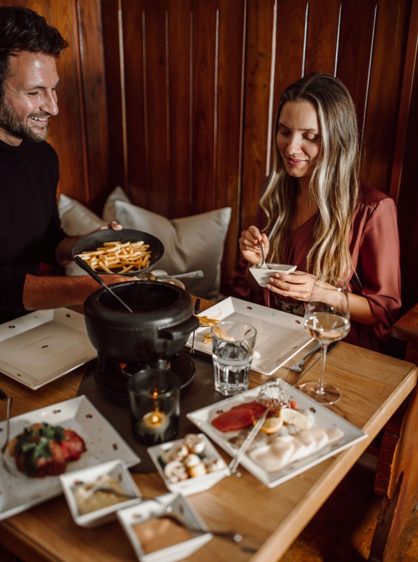 Zwei Personen genießen ein Fondue zusammen an einem Tisch mit verschiedenen Beilagen