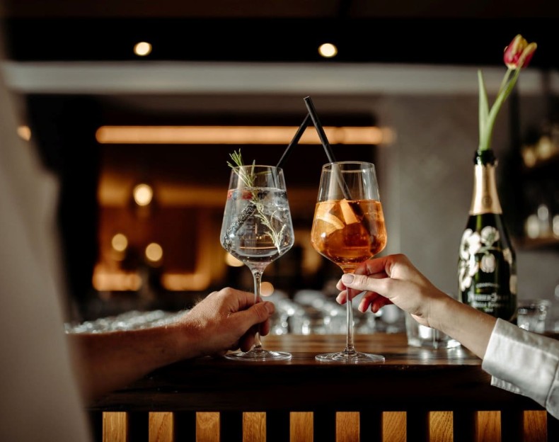 Zwei Personen stoßen mit Cocktails an einer Bar an