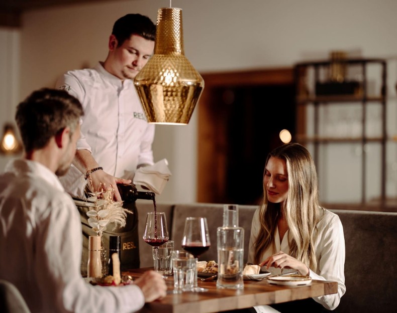 Kellner schenkt Rotwein für ein Paar in stilvollen Restaurant 1774 in Flachau